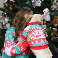 una mujer en pijama sosteniendo un perro con un suéter navideño