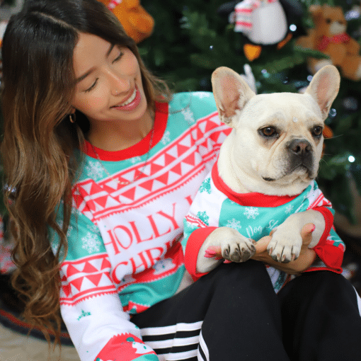 una mujer sosteniendo un perro pequeño frente a un árbol de navidad