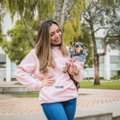 una mujer con un suéter rosa sosteniendo un perro pequeño